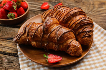 Plate of delicious croissants with chocolate and strawberry on wooden background