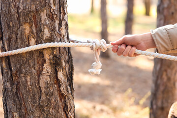 Male tourist tying rope to tree in forest
