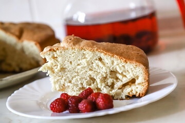 Piece of the homemade apple pie on the white plate served with some raspberries