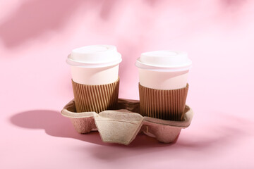 Holder with takeaway paper cups on pink background