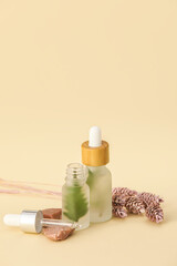 Bottles of natural serum and flowers on beige background