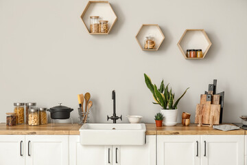 Fototapeta na wymiar White counters with sink, food, kitchen utensils and houseplants near light wall
