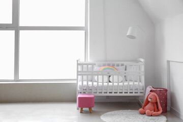 Interior of light nursery with baby crib, lamp and pouf