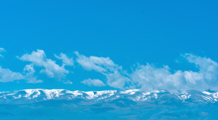 blue mountain sky landscape, snowy peaks of a mountain range in the distance under a clear sky with clouds
