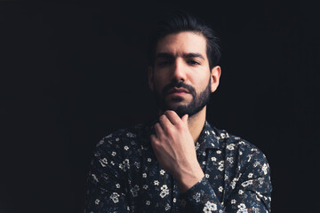 bearded Latin American handsome male person touching his chin looking severely into the camera copy space black background studio shot medium closeup. High quality photo