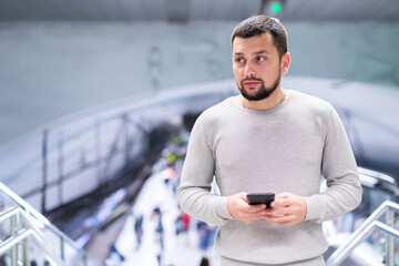 Young bearded man using his smartphone to check schedule while waiting for train on subway station platform ..