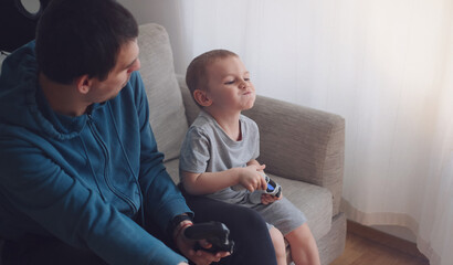 Happy father and son sit in the living room on the sofa and play or watch TV