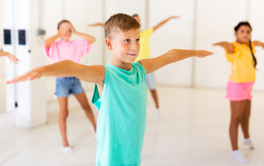 Smiling preteen boy doing stretching workout with group of children before dance training in...