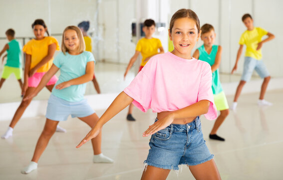 Happy tween girl dancing with children during group class in modern choreographic studio.