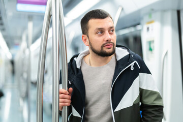 Portrait of thoughtful young bearded man holding on handrails in subway car during daily commute to...