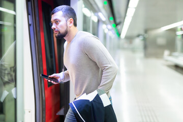 Young bearded man with jacket in hand boarding modern subway car. Concept of daily city commuting..