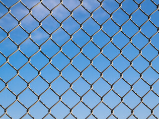 Fototapeta premium Fence with metal grid in perspective. Metal fence Part of a metal grid fence in blue sky at the background