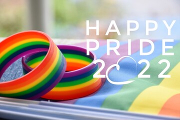 'Happy PRIDE 2022', and rainbow wristband, symbol of lgbt, on blurred rainbow flags background,...