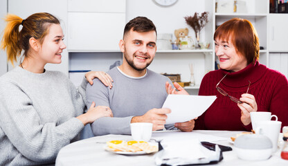 Cheerful senior woman with adult children looking at papers analyzing their finances at home