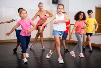 Sporty ten years old girl training movements of vigorous dance during group class in dance school..