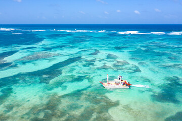 Boat floating in caribbean sea with reef and turquoise water, tropical holidays. Aerial view