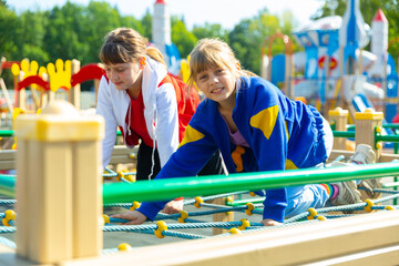 Happy girls play on ropes at playground area in summer