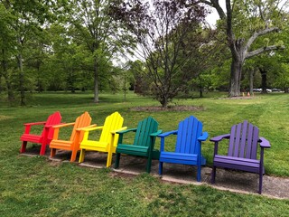 A rainbow set of adirondack chairs in a park.