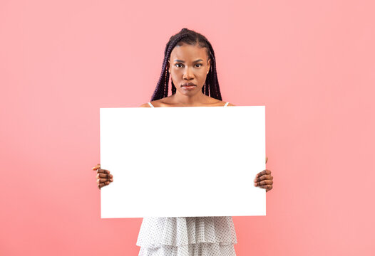 Serious young black woman holding empty paper banner with mockup for design on pink background