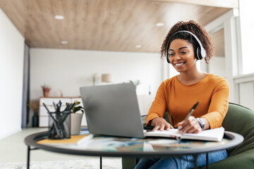 Woman sitting at desk, using computer and writing in notebook