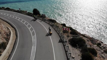 Drone Flying Over The Couple Riding Bicycles With Trailers On The Highway Between The Rocks And The Sea