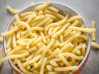 Closeup of Italian food yellow raw uncooked vermicelli, macaroni, noodle, pastry, pasta on the isolated bowl (close-up,meal, cuisine, cooking, gray, dry, dish, studio, plate,dinner, tile, cement)