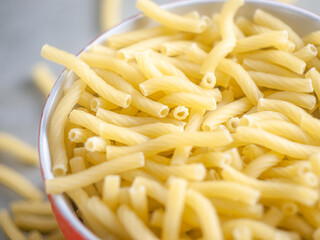 Closeup of Italian food yellow raw uncooked vermicelli, macaroni, noodle, pastry, pasta on the isolated red bowl (close-up,meal, cuisine, cooking, gray, dry, dish, studio, plate,dinner, tile, cement)