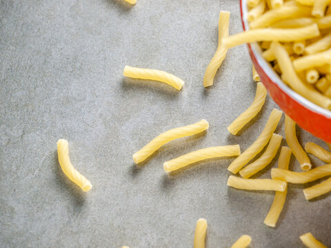 Closeup of Italian food yellow raw uncooked vermicelli, macaroni, noodle, pastry, pasta on the isolated bowl (close-up,meal, cuisine, cooking, gray, dry, dish, studio, plate,dinner, tile, cement)
