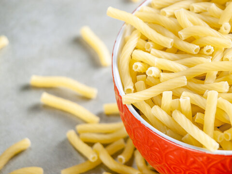 Closeup of Italian food yellow raw uncooked vermicelli, macaroni, noodle, pastry, pasta on the isolated bowl (close-up,meal, cuisine, cooking, gray, dry, dish, studio, plate,dinner, tile, cement)