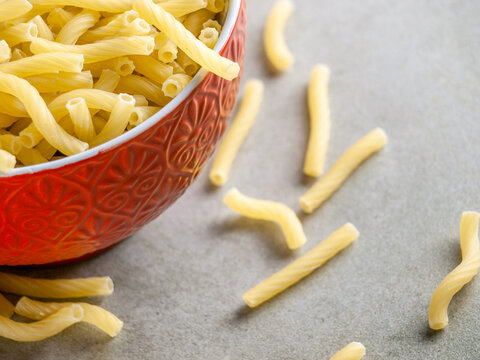 Closeup of Italian food yellow raw uncooked vermicelli, macaroni, noodle, pastry, pasta on isolated gray cement (close-up, meal, cuisine, cooking, gray, dry, dish, studio, plate, dinner, tile, cement)