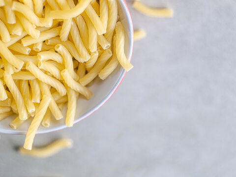 Closeup of Italian food yellow raw uncooked vermicelli, macaroni, noodle, pastry, pasta on the isolated red bowl (close-up,meal, cuisine, cooking, gray, dry, dish, studio, plate,dinner, tile, cement)