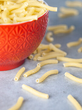 Closeup of Italian food yellow raw uncooked vermicelli, macaroni, noodle, pastry, pasta on the isolated red bowl (close-up,meal, cuisine, cooking, gray, dry, dish, studio, plate,dinner, tile, cement)