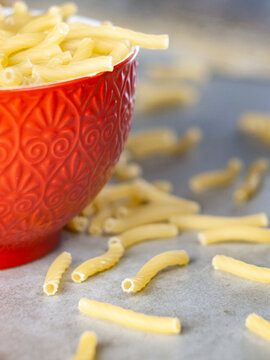 Closeup of Italian food yellow raw uncooked vermicelli, macaroni, noodle, pastry, pasta on the isolated red bowl (close-up,meal, cuisine, cooking, gray, dry, dish, studio, plate,dinner, tile, cement)
