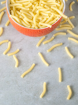 Closeup of Italian food yellow raw uncooked vermicelli, macaroni, noodle, pastry, pasta on the isolated red bowl (close-up,meal, cuisine, cooking, gray, dry, dish, studio, plate,dinner, tile, cement)