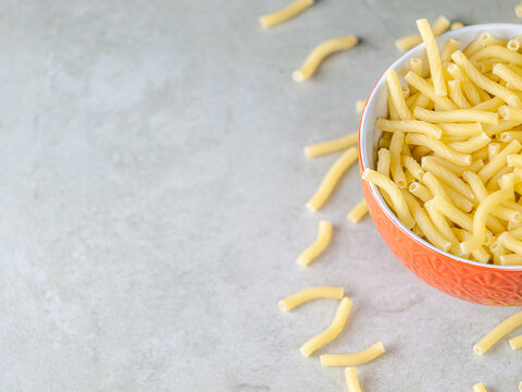Closeup of Italian food yellow raw uncooked vermicelli, macaroni, noodle, pastry, pasta on the isolated red bowl (close-up,meal, cuisine, cooking, gray, dry, dish, studio, plate,dinner, tile, cement)