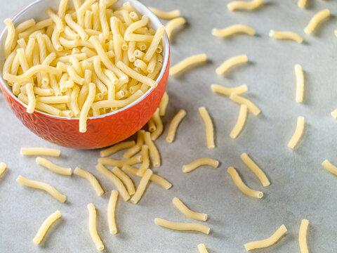 Closeup of Italian food yellow raw uncooked vermicelli, macaroni, noodle, pastry, pasta on the isolated red bowl (close-up,meal, cuisine, cooking, gray, dry, dish, studio, plate,dinner, tile, cement)