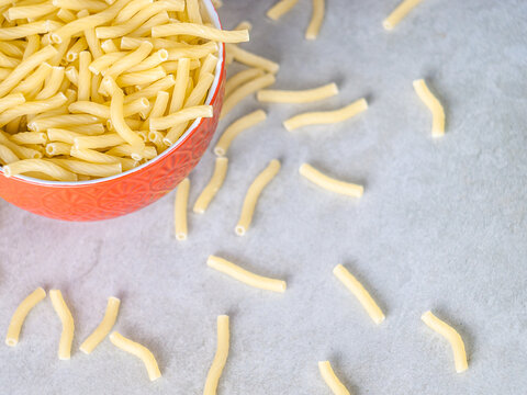 Closeup of Italian food yellow raw uncooked vermicelli, macaroni, noodle, pastry, pasta on the isolated red bowl (close-up,meal, cuisine, cooking, gray, dry, dish, studio, plate,dinner, tile, cement)