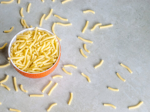 Closeup of Italian food yellow raw uncooked vermicelli, macaroni, noodle, pastry, pasta on the isolated red bowl (close-up,meal, cuisine, cooking, gray, dry, dish, studio, plate,dinner, tile, cement)