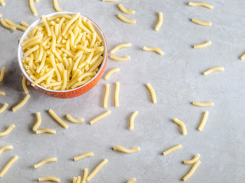 Closeup of Italian food yellow raw uncooked vermicelli, macaroni, noodle, pastry, pasta on the isolated red bowl (close-up,meal, cuisine, cooking, gray, dry, dish, studio, plate,dinner, tile, cement)