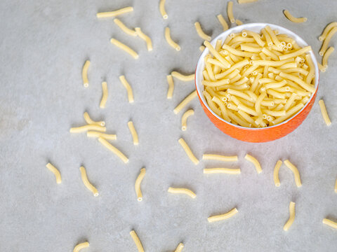 Closeup of Italian food yellow raw uncooked vermicelli, macaroni, noodle, pastry, pasta on the isolated red bowl (close-up,meal, cuisine, cooking, gray, dry, dish, studio, plate,dinner, tile, cement)