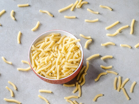 Closeup of Italian food yellow raw uncooked vermicelli, macaroni, noodle, pastry, pasta on the isolated red bowl (close-up,meal, cuisine, cooking, gray, dry, dish, studio, plate,dinner, tile, cement)