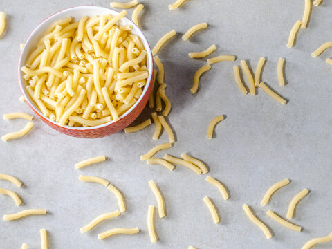 Closeup of Italian food yellow raw uncooked vermicelli, macaroni, noodle, pastry, pasta on the isolated red bowl (close-up,meal, cuisine, cooking, gray, dry, dish, studio, plate,dinner, tile, cement)