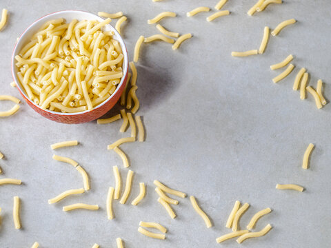 Closeup of Italian food yellow raw uncooked vermicelli, macaroni, noodle, pastry, pasta on the isolated red bowl (close-up,meal, cuisine, cooking, gray, dry, dish, studio, plate,dinner, tile, cement)