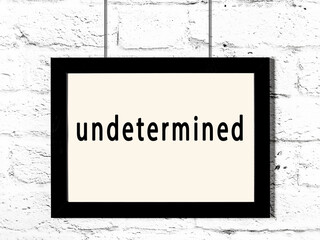 Black frame hanging on white brick wall with inscription undetermined - obrazy, fototapety, plakaty