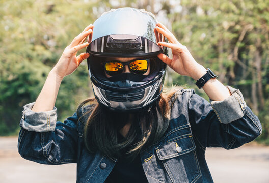 Young biker woman wearing a motorcycle helmet before riding a motorcycle.  Helmets contribute to motorcycle safety by protecting the rider's head.  Stock Photo | Adobe Stock