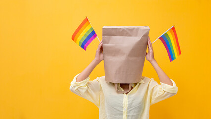 Portrait of shy LGBTQ people covering her face waving rainbow flag for coming out of the closet in...