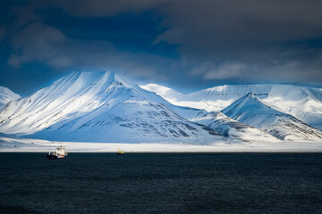 2022-05-08 SNOW COVERED MOUNTAINS OUTSIDE OF LONGYEARBYEN ON THE ISLAND OF SVALBARD NORWAY IN THE ARCTIC WITH A NICE BLUE CLOUDY SKY AND TWO SHIPS IN THE WATER