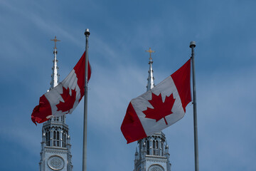 Two Canadian flags waving against blue sky in front of Catholic Church towers. - obrazy, fototapety, plakaty