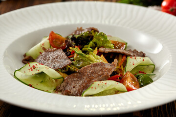 Steak salad with zucchini, tomatoes and lettuce on white plate. Fresh salad with roast beef and vegetables on wooden table in rustic style. Meat and vegetables salad on dark wooden background.