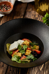 Salad with crispy eggplant, feta cheese and tomatoes on black plate. Fresh salad with eggplant and vegetables on wooden table in rustic style. aubergine and feta salad on dark wooden background.